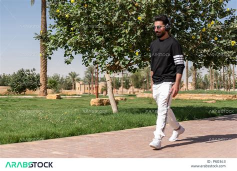 شاب عربي خليجي سعودي يرتدي النظارات الشمسية وسماعات الرأس الصوتية ويقضي وقت ممتع في الهواء الطلق