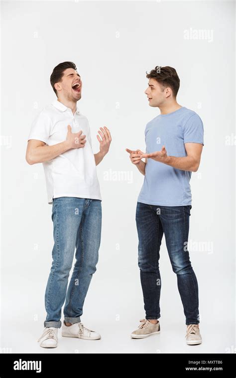 Full Length Portrait Of Two Handsome Young Men Talking And Laughing