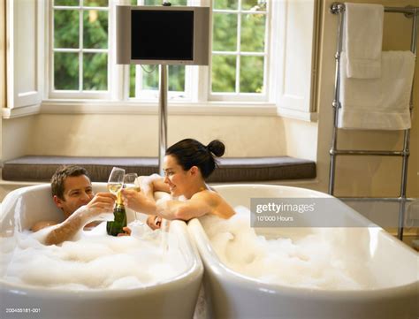 Couple In Adjacent Bubble Baths Toasting Champagne Glasses High Res