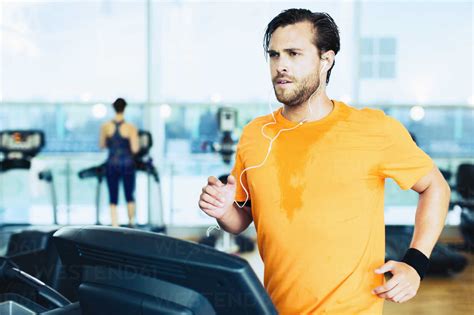 Sweating Man With Headphones Running On Treadmill At Gym Stock Photo