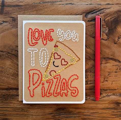 I Love You To Pizzas Embroidered On A Notebook With A Red Pen Next To It