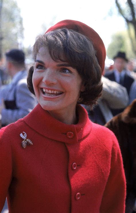 A Woman In A Red Coat And Hat Smiles At The Camera With Other People