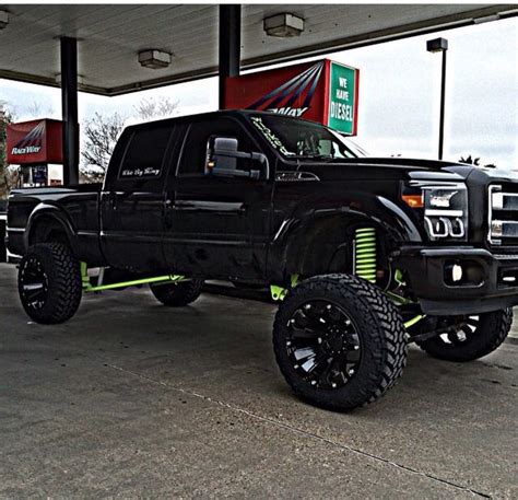 A Large Black Truck Parked In Front Of A Gas Station With Neon Green