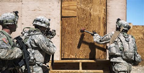 A Soldier Uses A Sledge Hammer To Break Down A Door To Gain Entry To A
