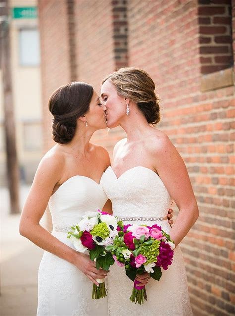 Two Brides Are Kissing Each Other In Front Of A Brick Wall And Holding Bouquets