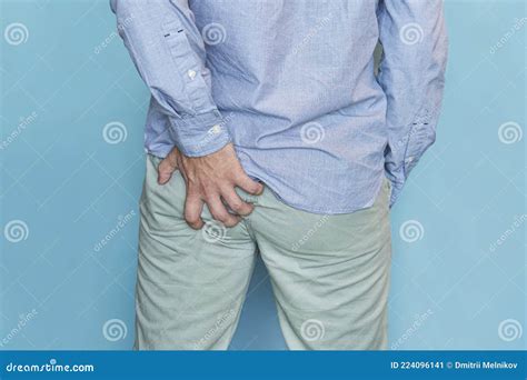 Man With Hemorrhoids Holding His In Pain In Blue Background Itching In The Anus Stock Image