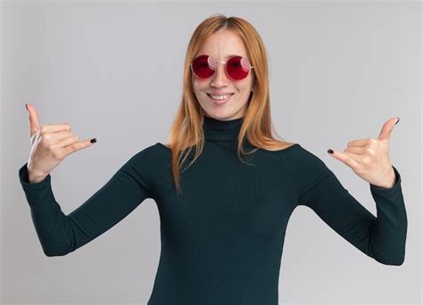 태양 안경에 주근깨가 있는 웃고 있는 어린 빨간 머리 생강 소녀는 복사 공간이 있는 흰 벽에 격리된 두 손으로 느슨한 몸짓을 하고 있다 무료 사진
