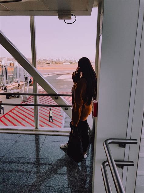 A Woman Standing In An Airport Looking Out The Window