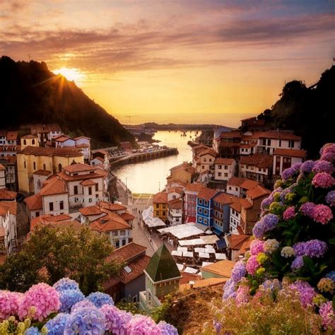 The Sun Is Setting Over An Old Town With Flowers In Front Of Water And