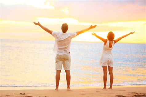Happy cheering couple enjoying sunset at beach with arms raised - Men ...