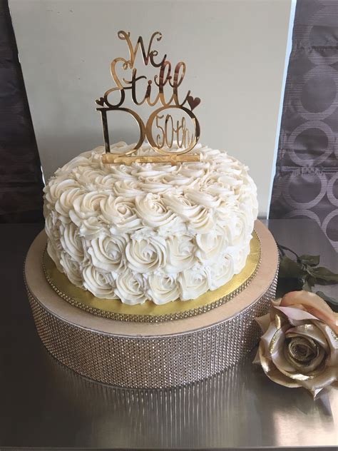 A Cake With White Frosting And Gold Trimmings Sits On A Table Next To A