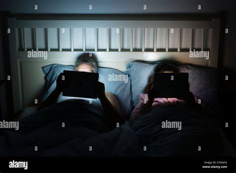 Couple Together In Bed At Night Both Using Ipad Tablet Computers Stock