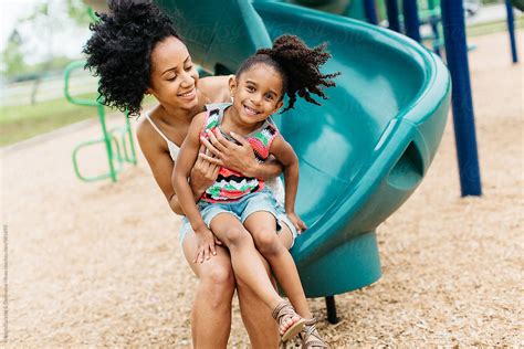 A Mother And Daughter Sitting Down On A Slide At The Playground By
