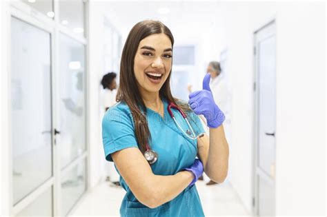 Portrait Of Smiling Female Doctor Wearing Scrubs In Busy Hospital