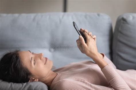 Pretty Young Woman Lying On Sofa With Smartphone Gadget Stock Image