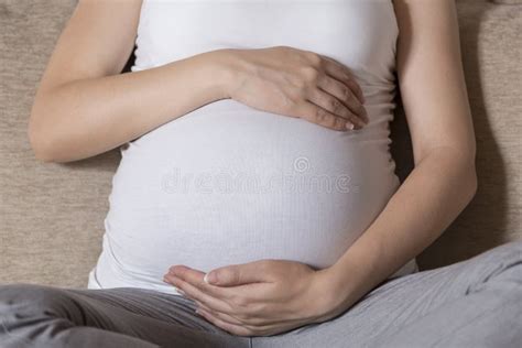 Close Up Of Pregnant Woman Sitting On Couch Touching Her Belly Stock