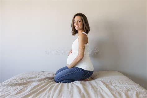 Attractive Pregnant Woman Is Sitting In Bed Holding Her Belly And