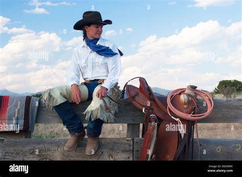Cowgirl Sitting On Corral Fence With Western Saddle On Ranch Stock