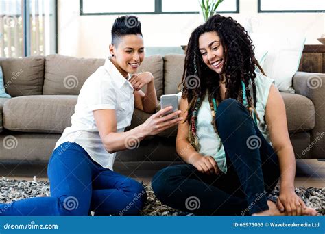 smiling lesbian couple sitting on rug and looking at their mobile phone stock image image of