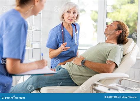 Man Sitting In Chair And Carefully Answers Mature Female Doctor