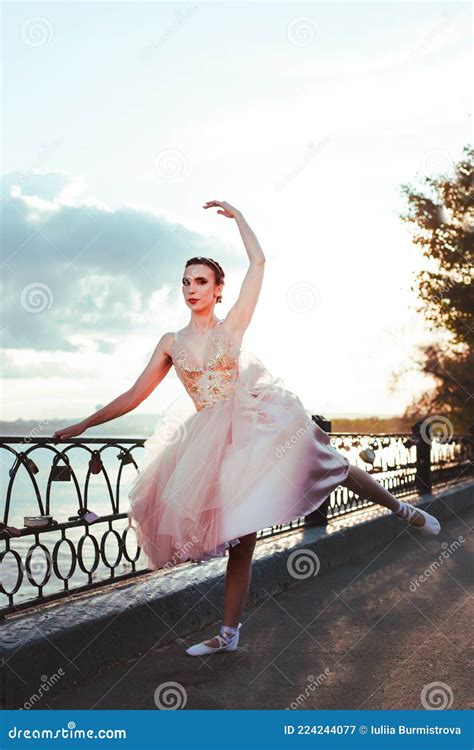A Thin Ballerina In A Pink Silk Corset Dress Gracefully Raises Her