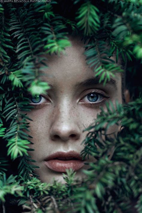 A Woman With Blue Eyes Hiding Behind Green Leaves