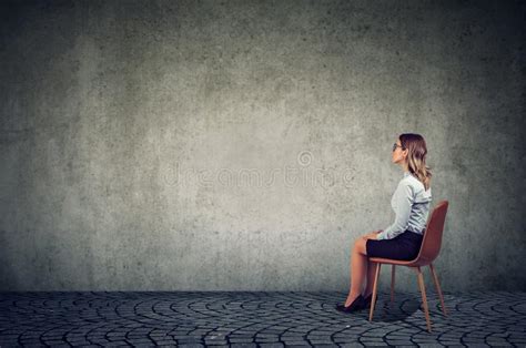 Business Woman Sitting On A Chair In Front Of A Wall And Thinking Stock