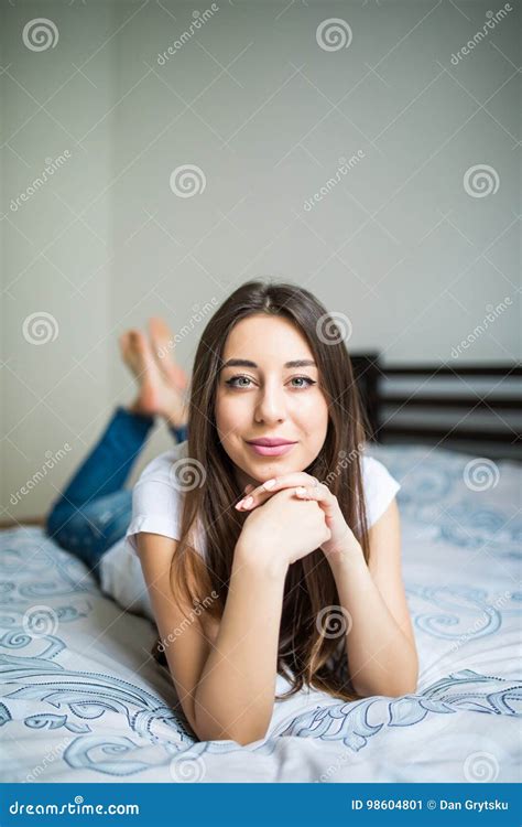 Young Woman Lying At The End Of The Bed Smiling With Her Head Resting