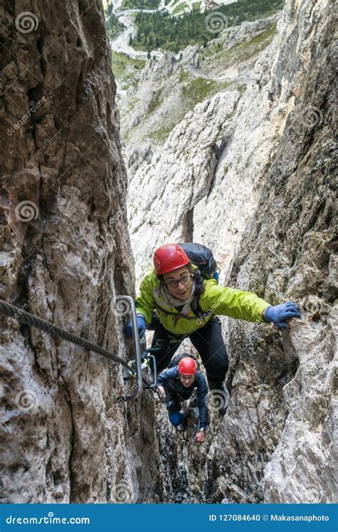 Two Young Female Mountain Climbers Climb Through A Narrow Crack On A