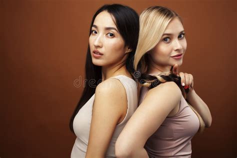 Two Pretty Diverse Girls Happy Posing Together Blond And Brunette Caucasian And Asian On Brown