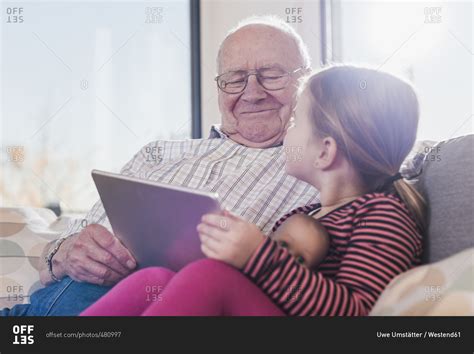 Grandfather Reading Out Story For His Granddaughter Using Ebook Stock