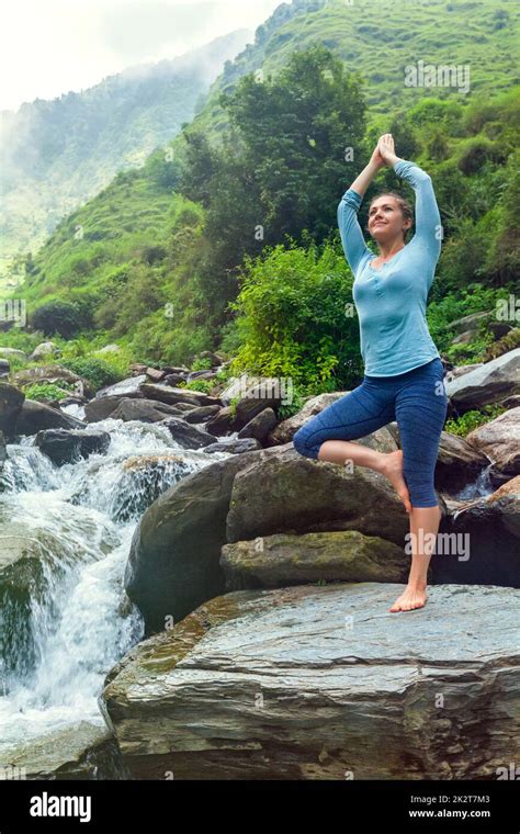 Woman In Yoga Asana Vrikshasana Tree Pose At Waterfall Outdoors Stock