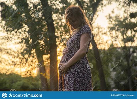 A Happy Pregnant Woman Standing In The City Park Holding Her Arms