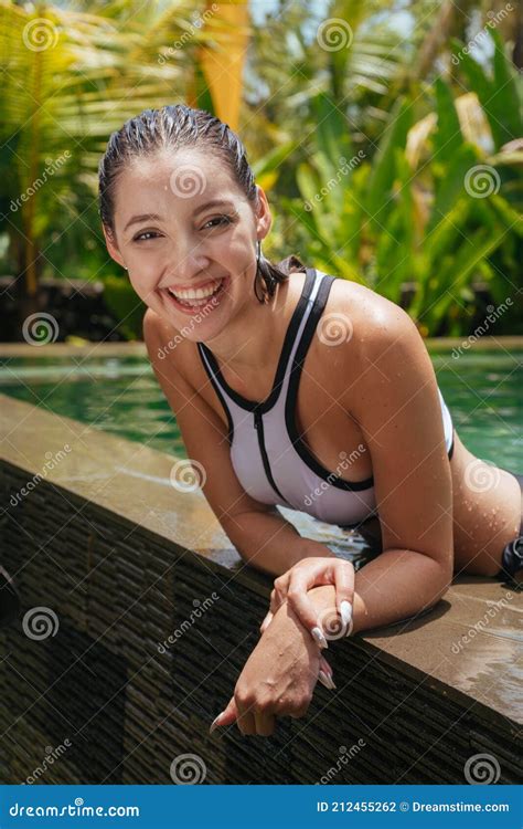 Leaning On The Edge Of The Pool The Beautiful Girl Smiles With A Broad