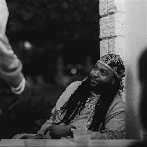 A Black And White Photo Of A Man With Dreadlocks Sitting At A Table
