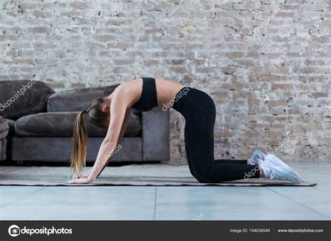 Fit Young Caucasian Woman Practicing Yoga At Home Standing In Cat And Cow Pose Arching Her Back