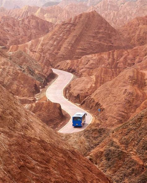 A Blue Truck Driving Down A Winding Road In The Middle Of Some