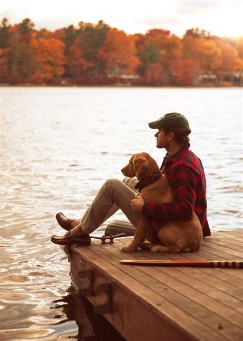 A Man Sitting On A Dock With His Dog