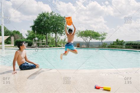 Boy Jumping Into A Swimming Pool While Another Teen Looks On Stock