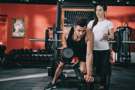 Attractive Trainer Instructing Young Sportsman Working Out Dumbbell