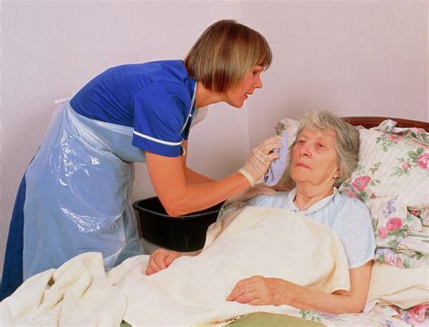 district nurse gives elderly patient a bed bath photograph by chris priest science photo library