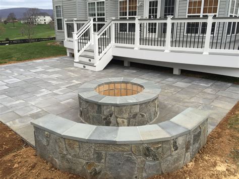 A Beautiful Paver Patio With Stone Seating Walls And A Fire Pit Behind