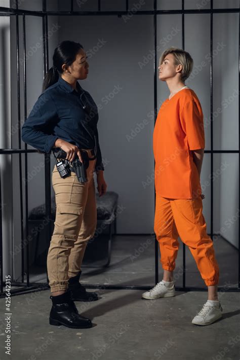 Asian Warden And A Female Prisoner In A High Security Prison Stand In Front Of An Open Cell 素材庫