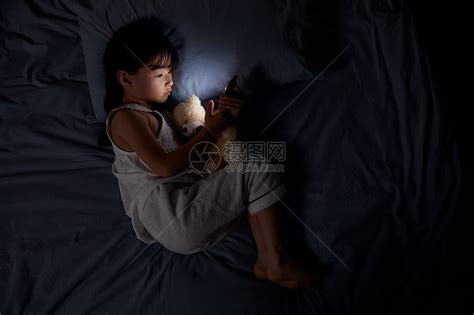 小女孩夜晚躺床上玩手机高清图片下载 正版图片501556314 摄图网