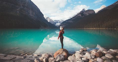 Person Standing On Rock In Front Of The Body Of Water And Mountains