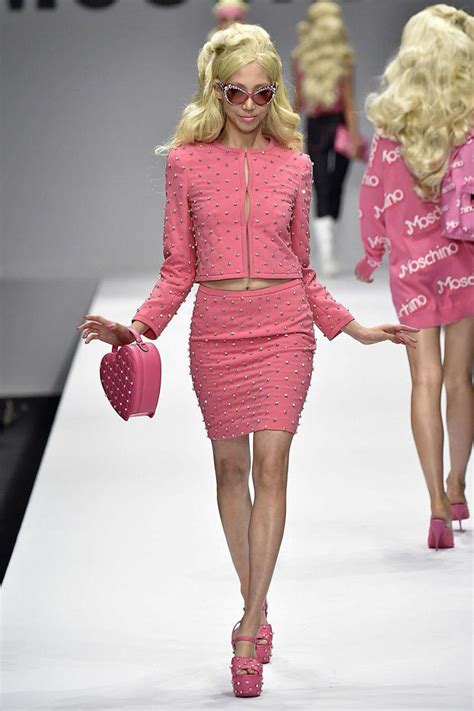 Two Models Walk Down The Runway In Pink Outfits And High Heels With One Holding A Handbag