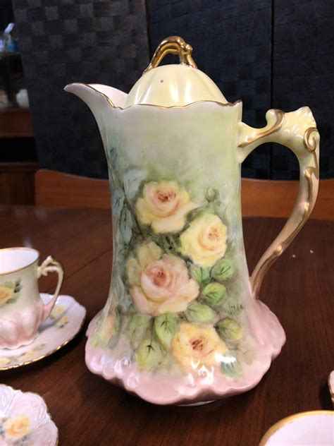 A Coffee Pot With Flowers Painted On It And Two Teacups Next To It