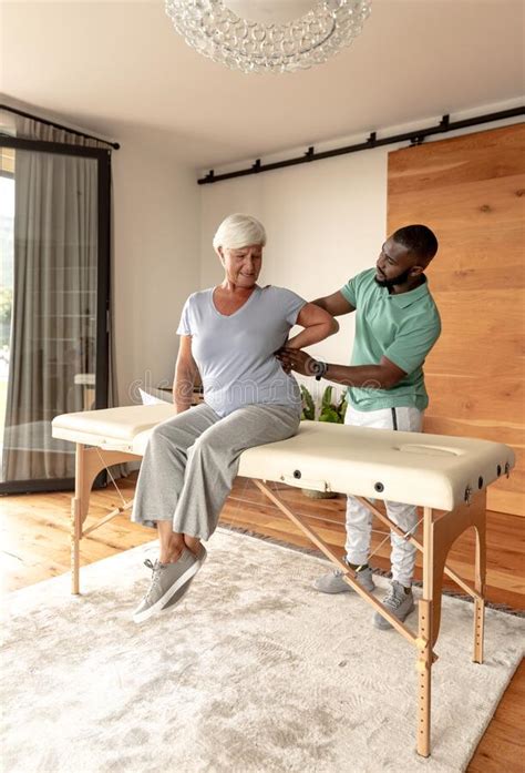African American Male Physiotherapist Giving Back Massage Therapy To Caucasian Senior Woman At