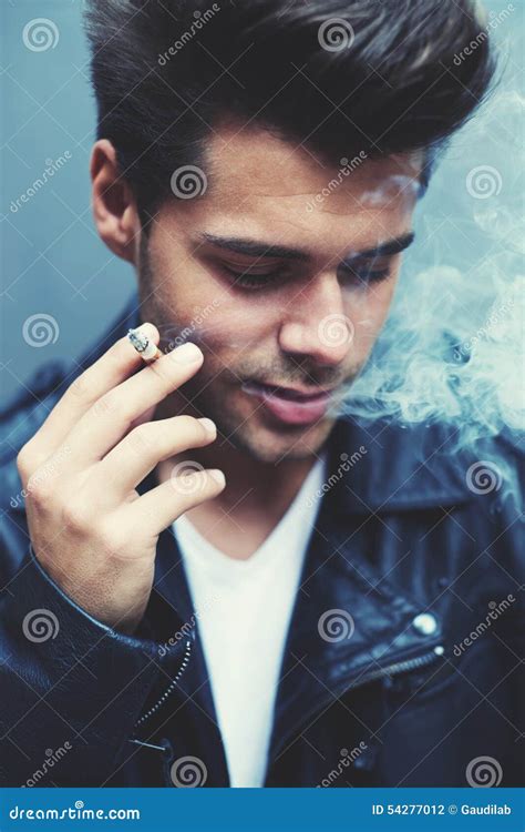Trendy Attractive Man Blowing Smoke Out Of His Mouth Standing On Grey