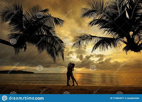 Silhouette Of Kissing Couple Standing On Tropical Beach During Sunset